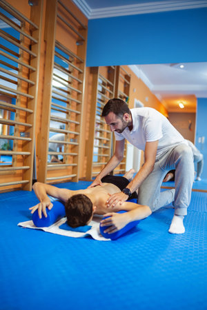 The boy is doing kinesiotherapy exercises with the chiropractor helping him. Exercises for correcting the spine and pelvis, scoliosis.の写真素材