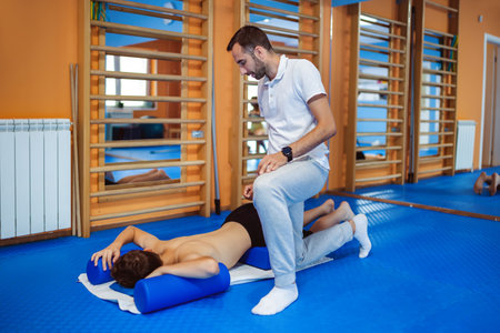The boy is doing kinesiotherapy exercises with the chiropractor helping him. Exercises for correcting the spine and pelvis, scoliosis.の写真素材