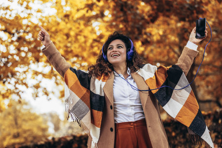 Relaxed Hispanic woman listening to music and breathing fresh air in autumn in a forest or parkの写真素材