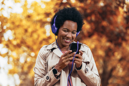 Relaxed African American woman listening to music and breathing fresh air in autumn in a forest or parkの写真素材