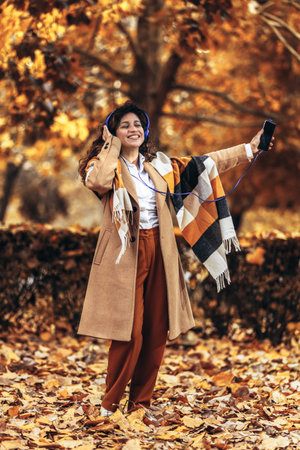 Relaxed Hispanic woman listening to music and breathing fresh air in autumn in a forest or parkの写真素材