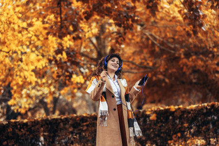 Relaxed Hispanic woman listening to music and breathing fresh air in autumn in a forest or parkの写真素材