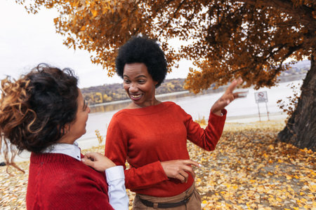 Two smiling young women friends jogging outside in the forest next to the lake in red sweatshirtsの写真素材