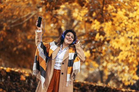 Relaxed Hispanic woman listening to music and breathing fresh air in autumn in a forest or parkの写真素材