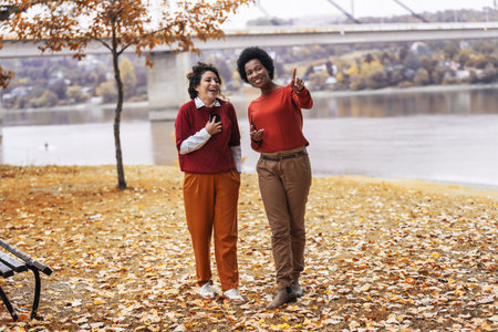 Two smiling young women friends jogging outside in the forest next to the lake in red sweatshirtsの写真素材