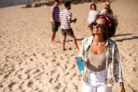 African American young woman drinking blue cocktail at he beach. Her friends are hanging out behind her.の写真素材