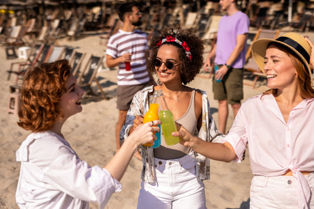 Three girl friends met at the beach to hang out. They are drinking cocktails and toasting.の写真素材