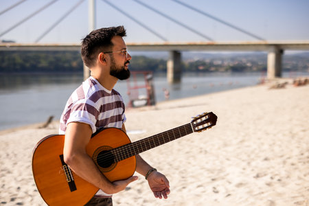 Guy at the beach brought his guitar. Walking on the sand on a sunny day.の写真素材