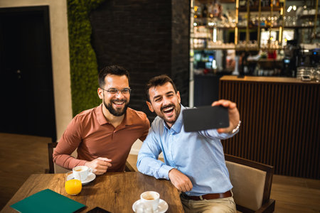 Two male friends hanging out at the coffee shop. Taking selfie with mobile phone.の写真素材