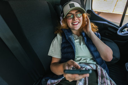 Young ginger woman truck driver taking a rest and uses her phone and headphones to listen to music.