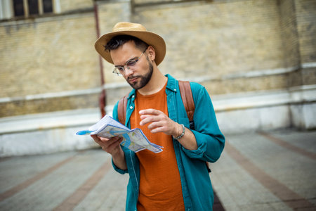 Male tourist with backpack and hat, looking at map while touring a foreign city.の写真素材