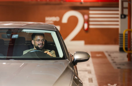 Young businessman searching for parking spot in underground garage. Driving around in his car.