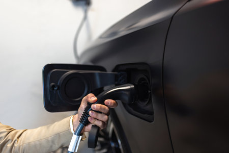 Young businessman at the charging station holding a plug to charge his electric car. Eco electric car conceptの写真素材
