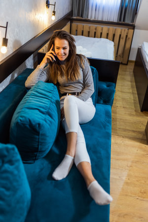 Portrait of nice girl sitting on blue couch and talking on her phone.の写真素材