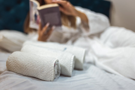 Closeup of towels in bed. Behind them is a girl reading a book in a bathrobe.の写真素材