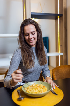 Woman eating mac and cheese in her apartmen.の写真素材