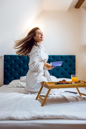 Pretty girl in the hotel room with bathrobe chilling and reading a book.の写真素材