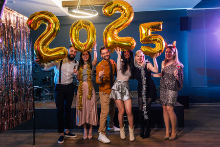 Group of friends celebrating New Years Eve 2025. They hold up gold balloon numbers.の写真素材