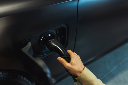 Young businessman at the charging station holding a plug to charge his electric car. Eco electric...