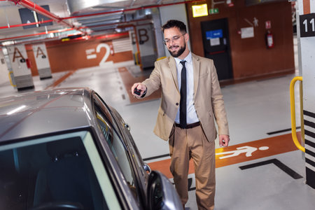 Young businessman unlocking his car with keys in an underground garage.