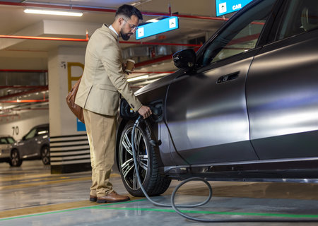 Young businessman at the charging station holding a plug to charge his electric car. Eco electric car conceptの写真素材