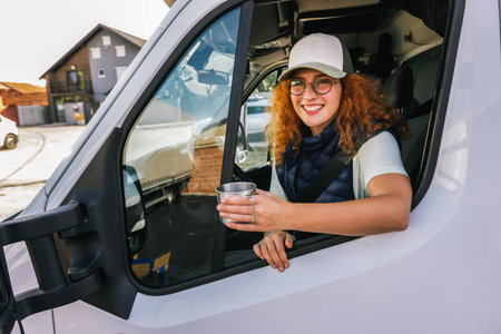 Young ginger woman driving long vehicle and drinking coffee so she could get some energy.の写真素材