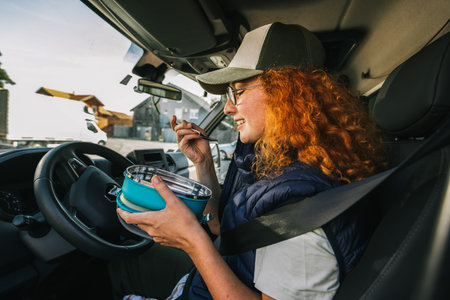 Ginger woman truck driver taking a break from long drive to eat some food from container.