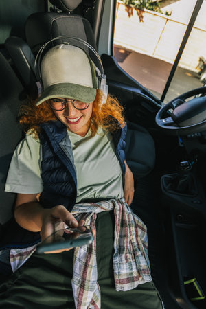Young ginger woman truck driver taking a rest and uses her phone and headphones to listen to music.