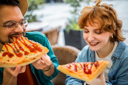 Couple in restaurant eats delicious looking pizza with ketchup.