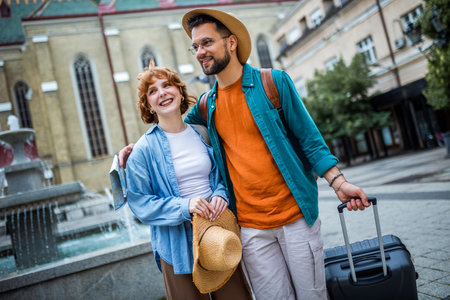 Young couple exploring the new city. Hugging and walking through the center. Wearing hats, backpacks and luggage.の写真素材