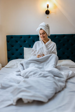 Woman in a hotel room. Wearing bathrobe and a towel on her head. Drinking hot drink after a bath.の写真素材