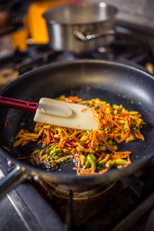Chef frying cut vegetables in pan in restaurant kitchen.の写真素材