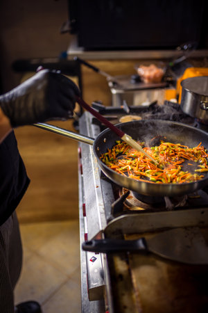 Chef frying cut vegetables in pan in restaurant kitchen.の写真素材
