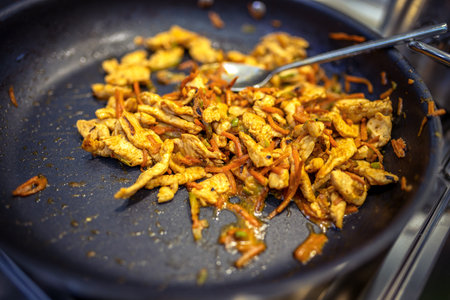 Chef frying cut vegetables and chicken in pan in restaurant kitchen.の写真素材
