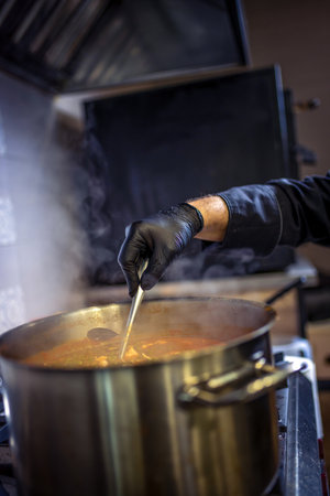 Chef in kitchen cooking in big pot green peas, beef, potatoes, onions with sauce.の写真素材