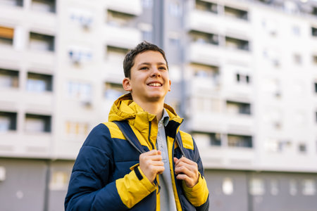 A young boy walking down a city street wearing a winter jacket and carrying a backpack on his shouldersの写真素材