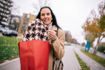 A middle-aged woman walking down the street, wearing a stylish coat and carrying shopping bagsの写真素材