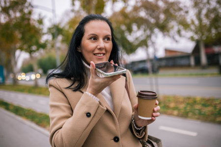 A middle-aged woman in a stylish coat, making a voice call on her smartphoneの写真素材