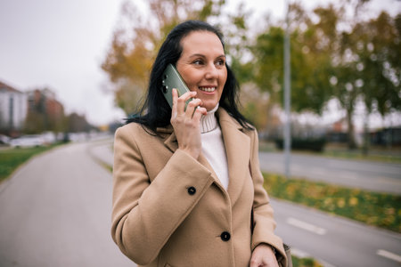 A middle-aged woman walking down the street in a stylish coat, talking on the phoneの写真素材