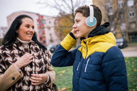 A young boy walking down a city street alongside his mother, both dressed in warm winter clothing. The boy and his mother are casually strolling together, with the mother guiding himの写真素材