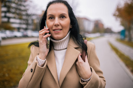 A middle-aged woman walking down the street in a stylish coat, talking on the phoneの写真素材