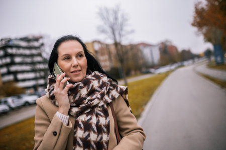 A middle-aged woman walking down the street in a stylish coat, talking on the phoneの写真素材
