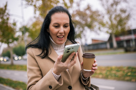 A middle-aged woman in a stylish coat, holding a coffee cup while speaking on the phoneの写真素材