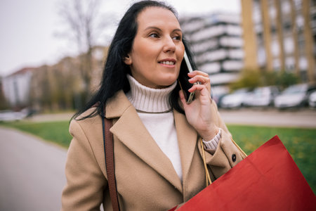 A middle-aged woman walking down the street in a stylish coat, talking on the phoneの写真素材