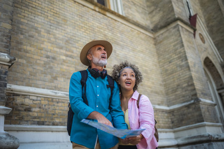 Portrait of happy senior couple tourists outdoors in historic town using map.の写真素材