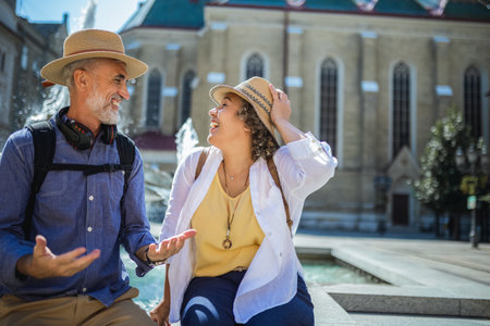 Senior couple of tourists stands happily in front of a stunning city fountain, surrounded by historic architectureの写真素材