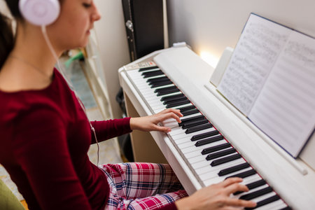 Young woman wearing headphones while playing the piano in her cozy room, deeply focused on her music.の写真素材