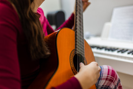 Young woman playing the guitar in her cozy room, with a piano positioned beside her.の写真素材