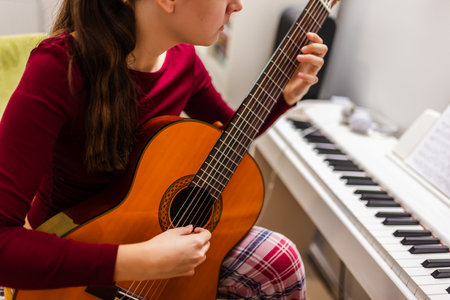 Young woman playing the guitar in her cozy room, with a piano positioned beside her.の写真素材