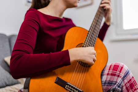 Young woman strumming her guitar in the comfort of her room.